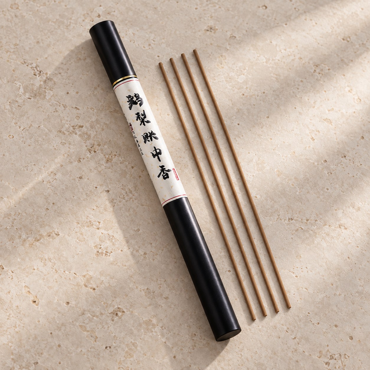 Black E Li Zhang Zhong incense tube beside four straight brown incense sticks on pale stone